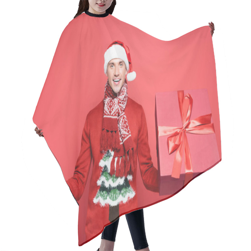 Personality  Positive Man In Sweater And Santa Hat Holding Gift Boxes On Red Background Hair Cutting Cape