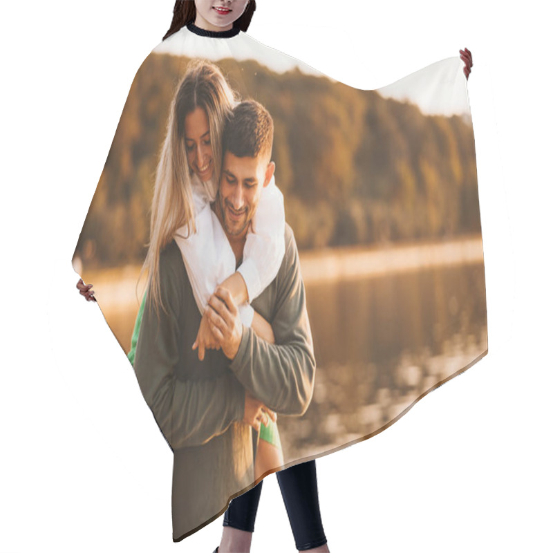 Personality  Cheerful Couple Is Having Fun While Man Is Holding Piggy Back His Woman Near A Lake. Hair Cutting Cape