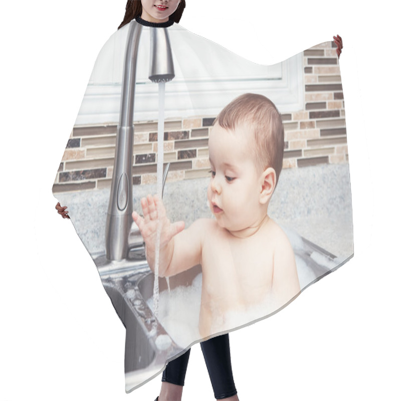 Personality  Portrait Of Cute Caucasian Funny Baby Girl Boy With Dark Black Eyes Sitting In Big Kitchen Sink With Water And Foam  Near Window Looking Away, Lifestyle Everyday Concept Hair Cutting Cape