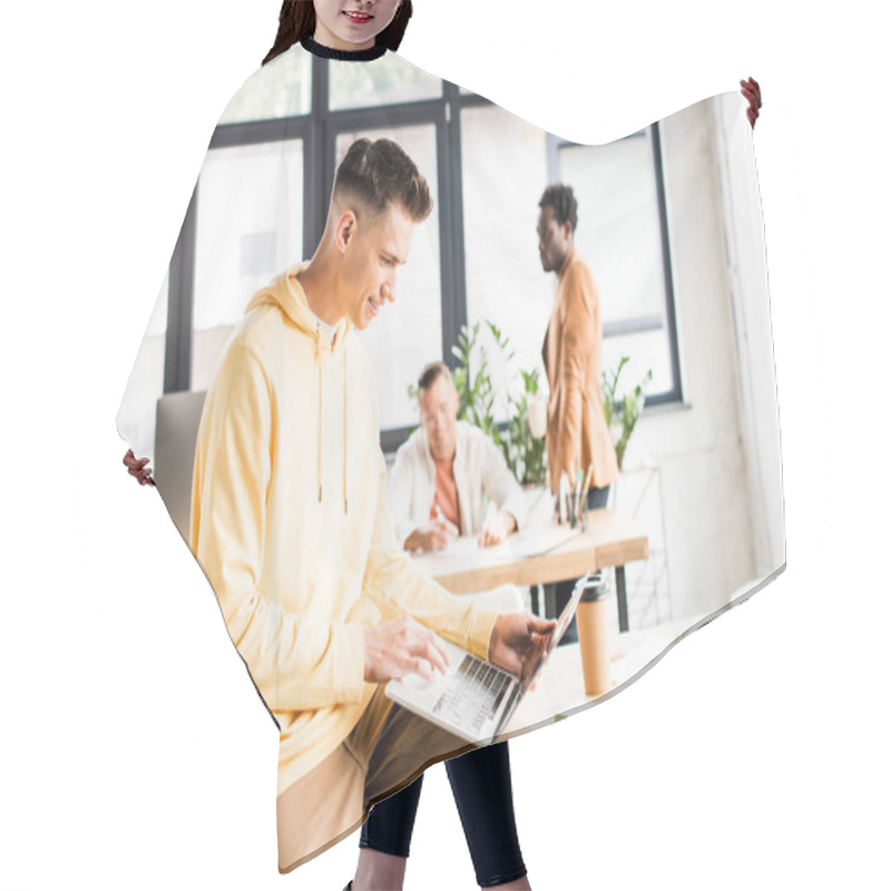 Personality  Young Businessman Using Laptop While Sitting On Desk In Office Near Multicultural Colleagues Hair Cutting Cape