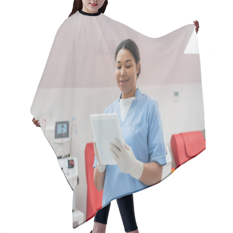 Personality  Smiling Multiracial Woman In Blue Uniform And Latex Gloves Using Digital Tablet Near Automated Transfusion Machine And Medical Chairs In Blood Transfusion Station Hair Cutting Cape