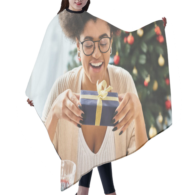 Personality  Joyous African American Woman Looking At Her Gift Smiling Cheerfully With Christmas Tree On Backdrop Hair Cutting Cape