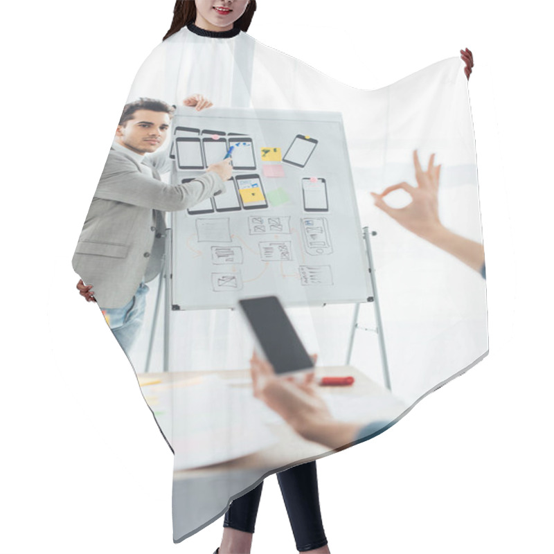 Personality  Selective Focus Of Ux Designer Near Whiteboard With Layouts Looking At Colleague With Smartphone Showing Okay Sing In Office  Hair Cutting Cape