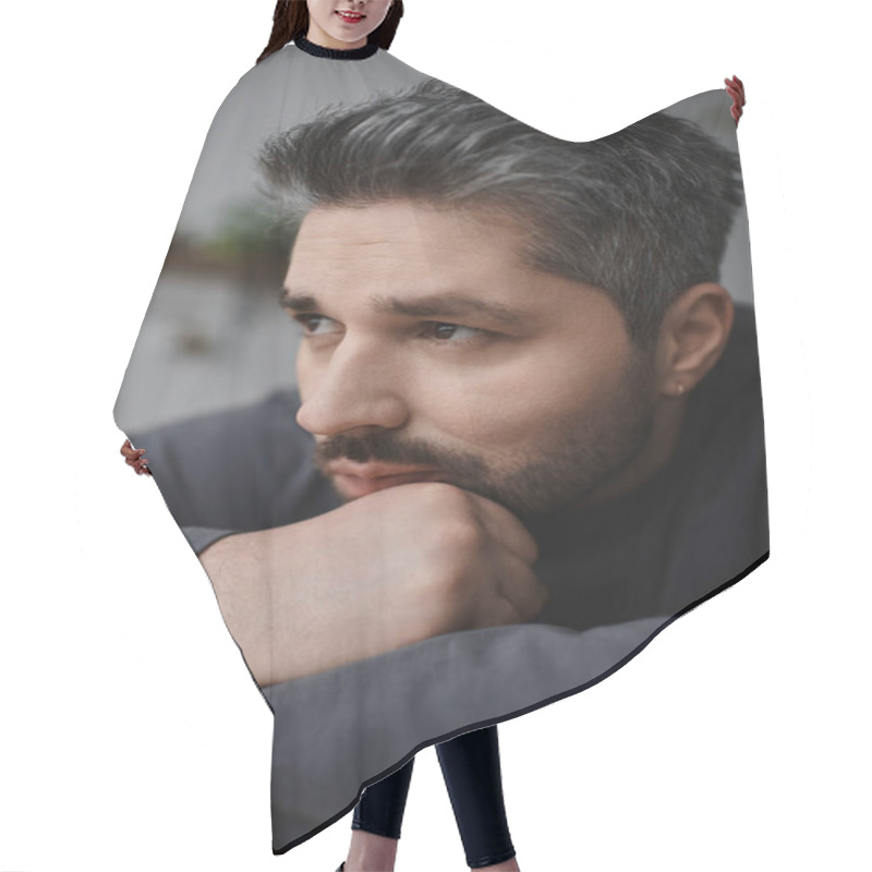 Personality  A Handsome Man Looks Thoughtful, Resting His Chin On His Hand In A Warm Setting. Hair Cutting Cape