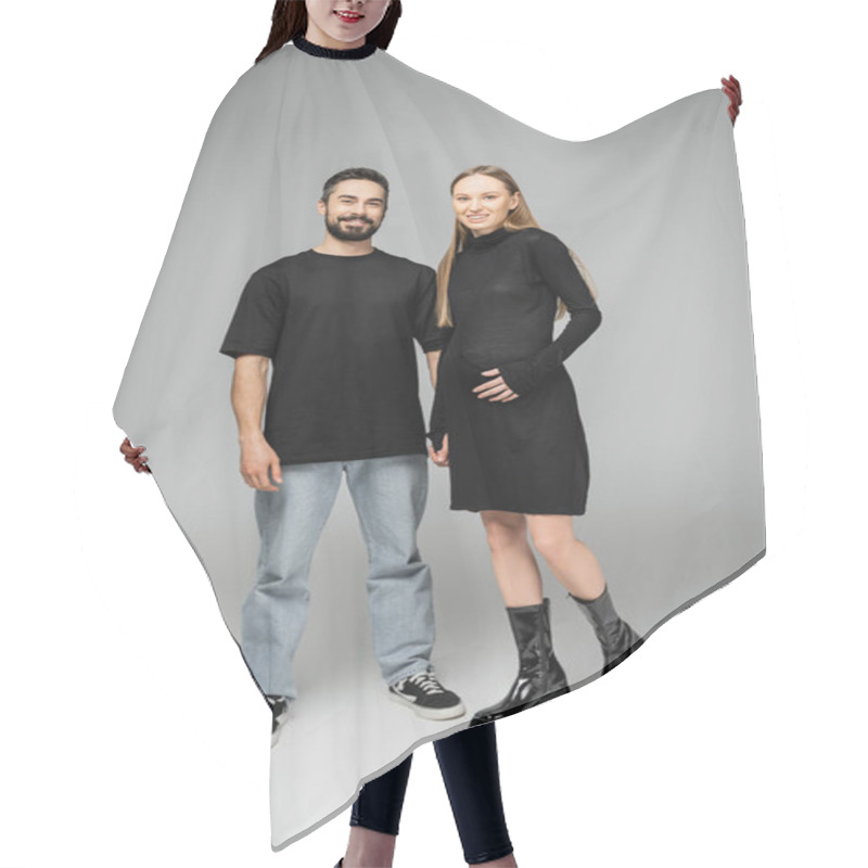 Personality  Full Length Of Cheerful And Trendy Pregnant Woman In Black Dress Looking At Camera While Standing Near Bearded Husband In T-shirt And Jeans On Grey Background, Concept Of Birth Of Child Hair Cutting Cape