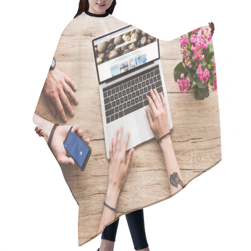 Personality  Cropped Shot Of Man With Smartphone With Facebook Logo In Hand And Woman At Tabletop With Laptop With Depositphotos Website And Kalanchoe Flower Hair Cutting Cape