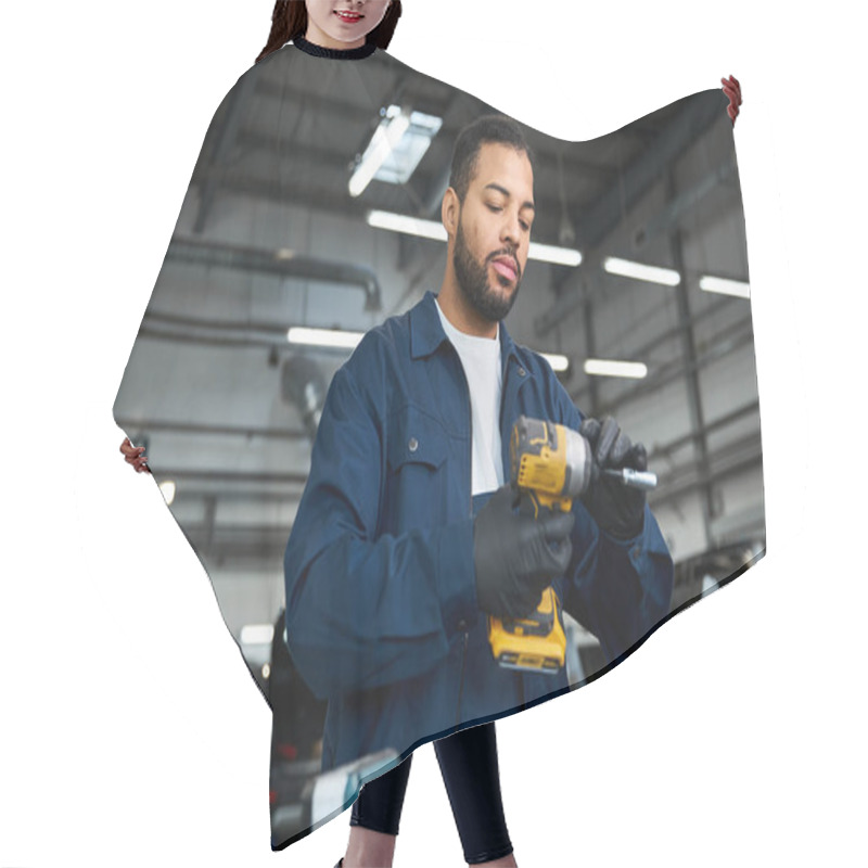 Personality  Handsome Young Mechanic Focuses Intently On A Power Tool In A Busy Garage Setting. Hair Cutting Cape