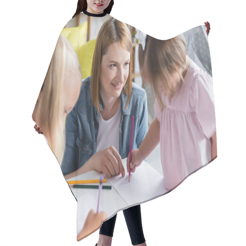 Personality  Smiling Kindergarten Teacher Looking At Blurred Toddler Kid With Down Syndrome Drawing With Preschooler Girl  Hair Cutting Cape