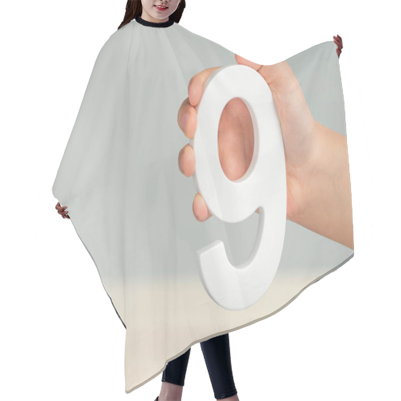 Personality  Number Nine In Hand. A Hand Holds A White Number 9 On A Blurred Background. Concept With Number Nine. Birthday 9 Years, Percentage, Ninth Grade Or Day Hair Cutting Cape