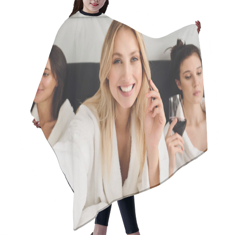 Personality  Young Pretty Cheerful Woman With Blond Hair In White Bathrobe Happily Looking In Camera With Eye Brush In Hand While Girls On Background Sitting With Wine In Bed In Modern Hotel Hair Cutting Cape