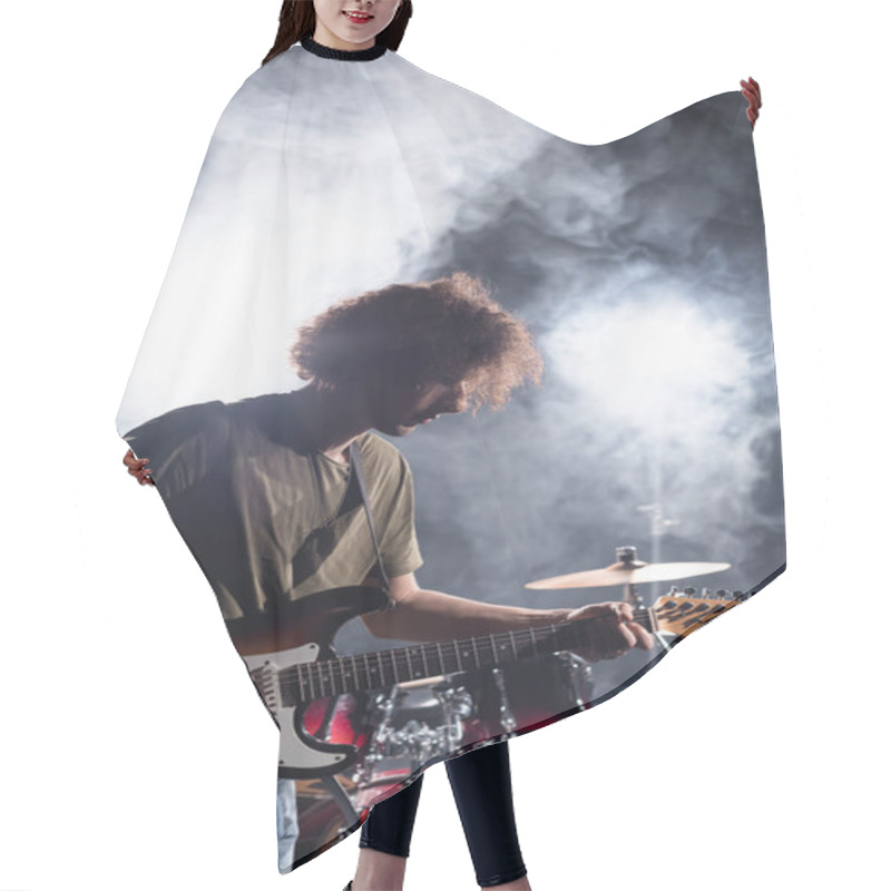 Personality  KYIV, UKRAINE - AUGUST 25, 2020: Rock Band Musician Playing Guitar With Pick Near Drum Kit With Smoke On Background Hair Cutting Cape