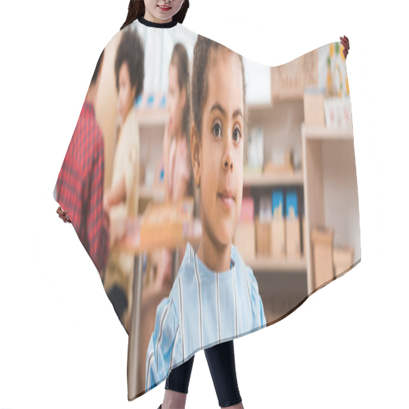 Personality  Selective Focus Of African American Kid Looking At Camera With Teacher And Children At Background In Montessori School Hair Cutting Cape