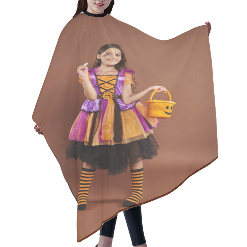 Personality  Lovely Girl In Halloween Costume Holding Bucket And Looking At Wrapped Candy On Brown Backdrop Hair Cutting Cape