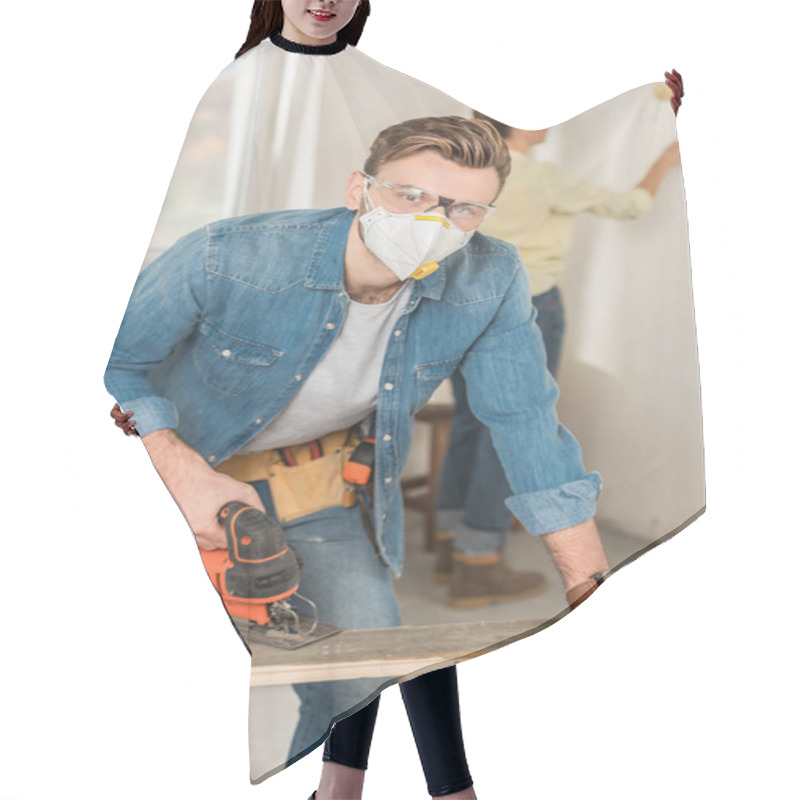 Personality  Young Man In Protective Workwear Using Electric Jigsaw And Looking At Camera Hair Cutting Cape