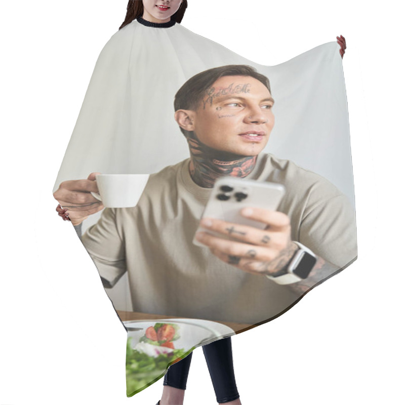 Personality  A Young Man Sips Coffee And Checks His Smartphone, Surrounded By A Fresh Salad At Home. Hair Cutting Cape