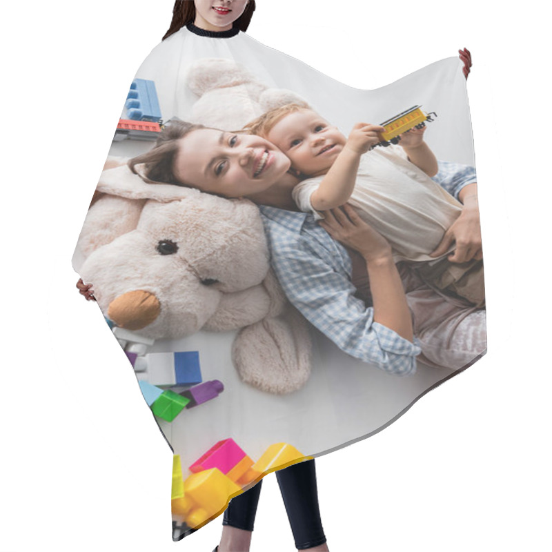 Personality  Top View Of Happy Woman Lying With Toddler Son On Toy Dog On Grey Hair Cutting Cape