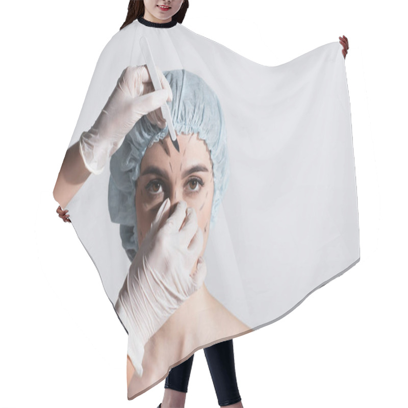 Personality  Plastic Surgeon In Latex Gloves Holding Scalpel Near Woman In Surgical Cap With Marked Lines On Face Isolated On Grey Hair Cutting Cape