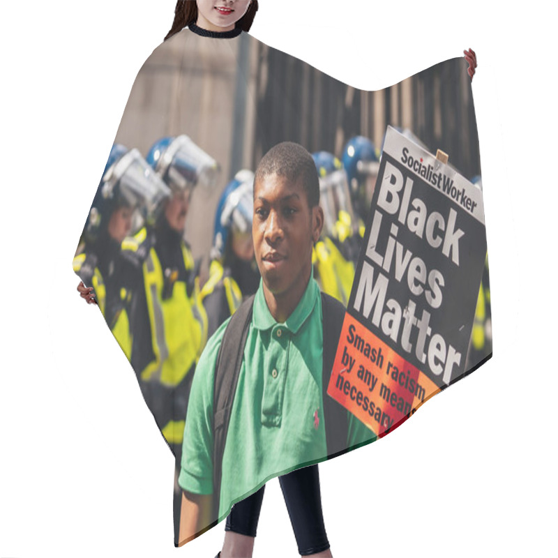 Personality  London / UK - 06/13/2020: Black Lives Matter Protest During Lockdown Coronavirus Pandemic. Young Man With BLM Banner Posing In Front Of Police Officers Hair Cutting Cape