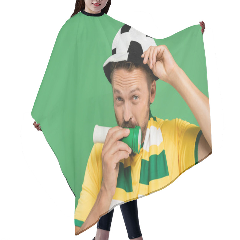 Personality  Bearded Man In Football Hat Blowing Horn While Looking At Camera Isolated On Green  Hair Cutting Cape