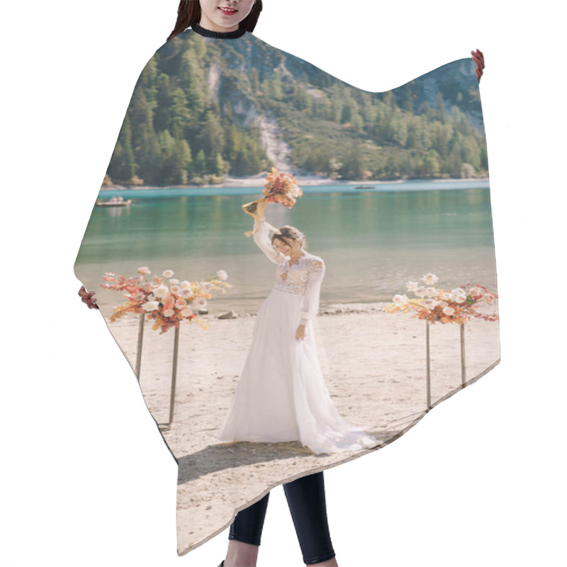 Personality  Beautiful Bride In A White Dress With Sleeves And Lace, With A Yellow Autumn Bouquet On Background Of The Arch For Ceremony, At Lago Di Braies In Italy. Destination Wedding In Europe, On Braies Lake. Hair Cutting Cape