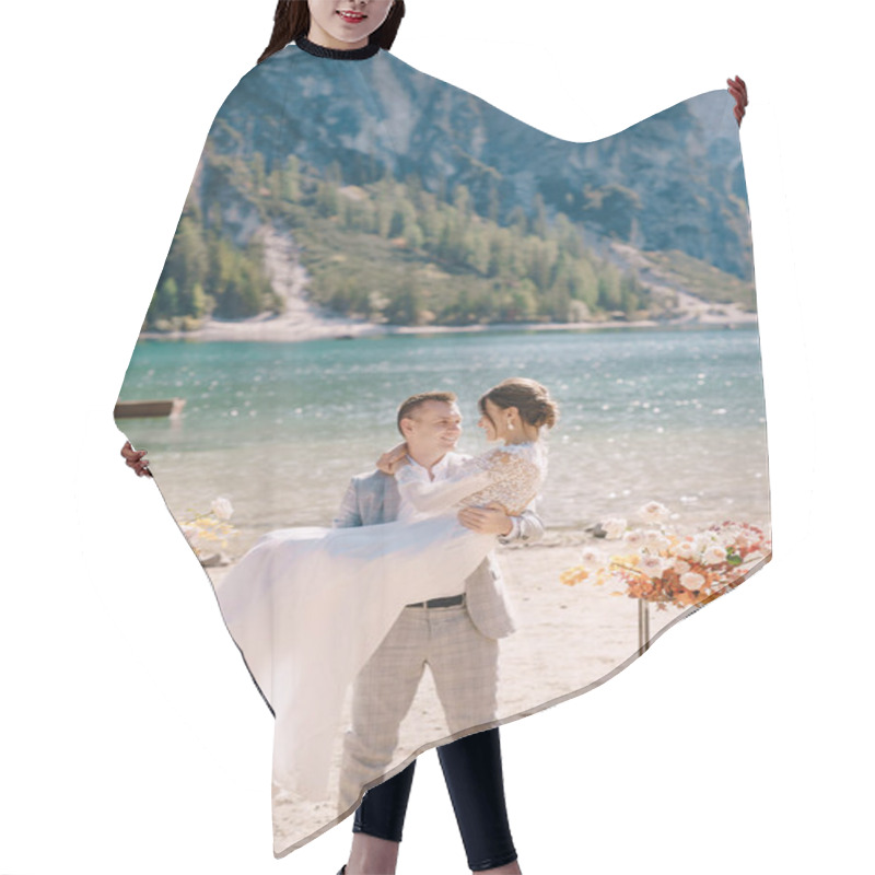 Personality  The Groom Circles The Bride In Her Arms At The Venue For Ceremony, With Two Autumn Flower Columns Instead Of An Arch, Against Backdrop Of Lago Di Braies In Italy. Wedding In Europe, On Braies Lake. Hair Cutting Cape