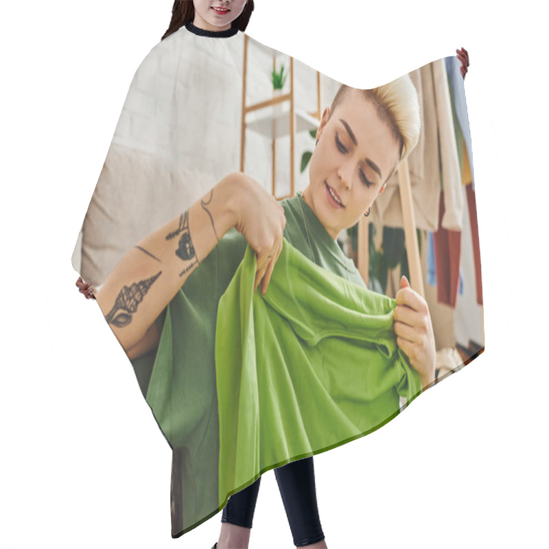 Personality  Pleased Woman Holding Green Garment Near Couch In Living Room While Decluttering Clothing At Home, Trendy Hairstyle, Tattoo, Sustainable Living And Mindful Consumerism Concept Hair Cutting Cape