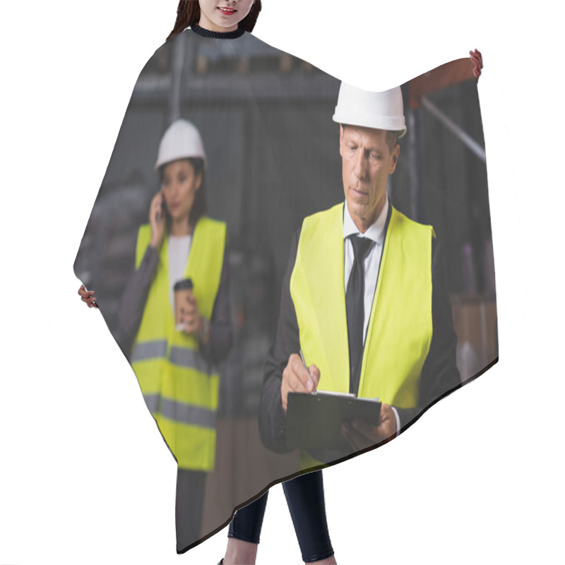 Personality  Warehouse Supervisor In Hard Hat Writing On Clipboard With Female Employee On Blurred Background Hair Cutting Cape