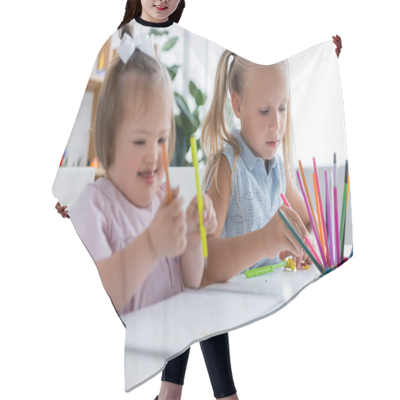 Personality  Girl Taking Pink Pencil Near Blurred Disabled Kid With Down Syndrome Hair Cutting Cape