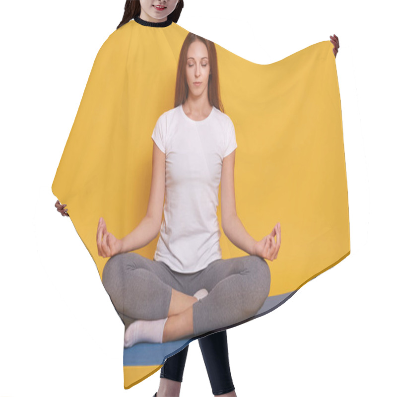 Personality  Studio Shot Of Young Woman Wearing White T Shirt And Gray Leggins, Sitting On Floor In Lotus Pose, Girl Holds Hands In Praying Gesture And Keeps Eyes Closed, Posing Isolated Over Yelow Background. Hair Cutting Cape