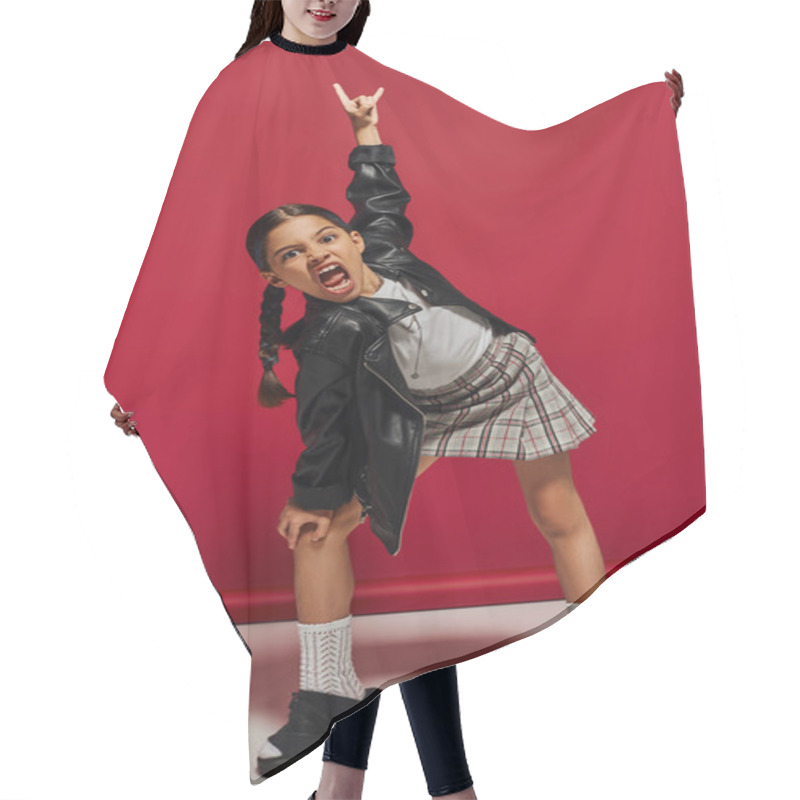 Personality  Mad And Trendy Preteen Girl With Hairstyle Wearing Leather Jacket And Plaid Skirt Looking At Camera And Showing Rock Gesture While Standing On Red Background, Stylish Preteen Outfit Concept Hair Cutting Cape