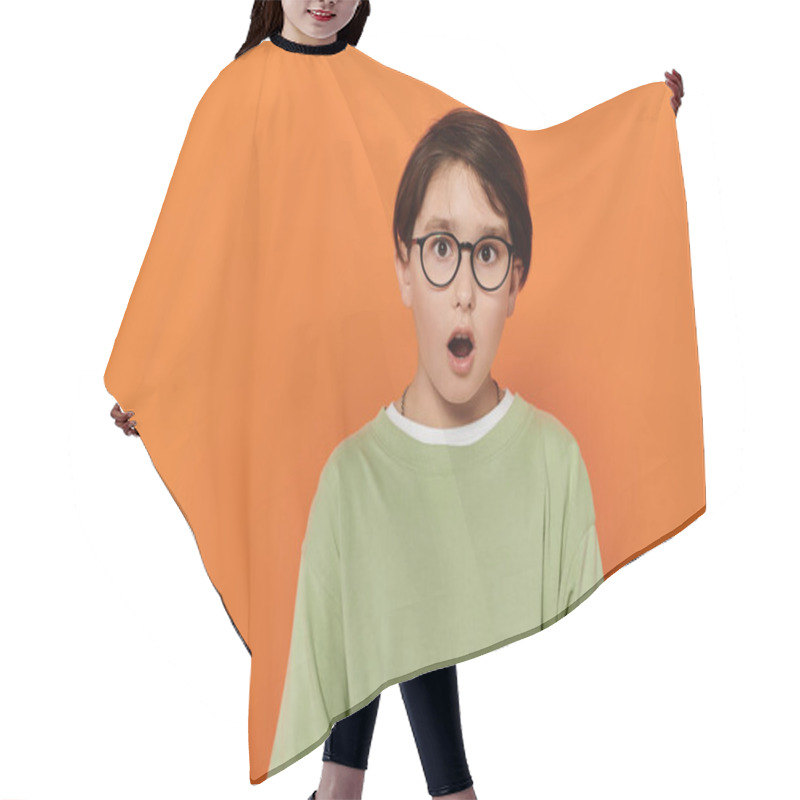 Personality  A Young Boy With Glasses Looks Surprised Against An Orange Backdrop. Hair Cutting Cape