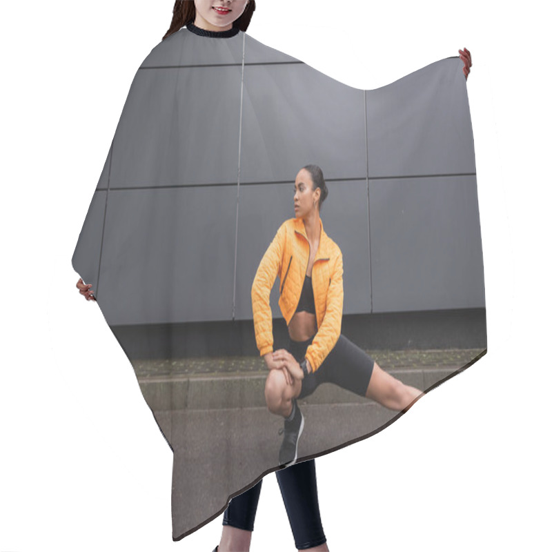 Personality  Full Length Of Stylish African American Sportswoman In Bike Shorts And Yellow Puffer Jacket Stretching Near Grey Building  Hair Cutting Cape