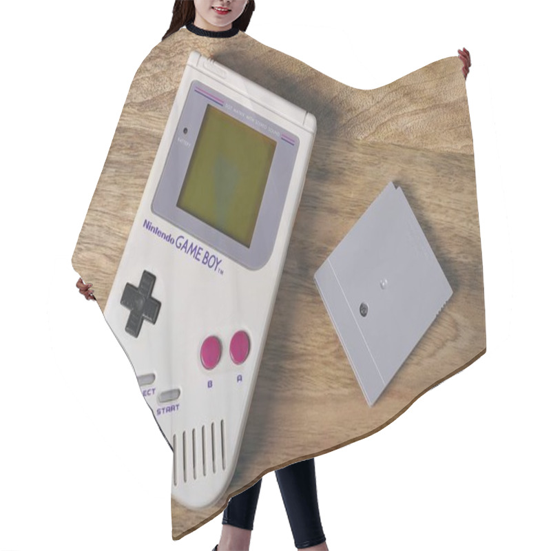 Personality  Neu-Ulm, Bavaria, Germany - April, 26, 2023: First Nintendo Game Boy Classic Edition Lying On The Table Next To A Game Cartridge. Hair Cutting Cape