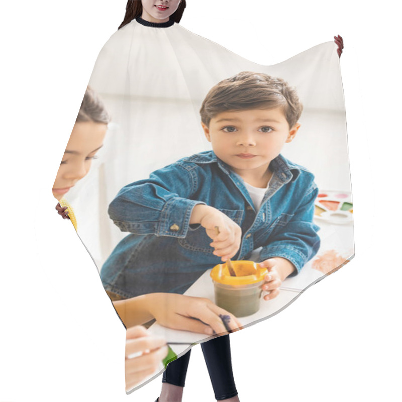 Personality  Adorable Boy Mixing Paints In Container While Sitting Near Sister And Looking At Camera Hair Cutting Cape