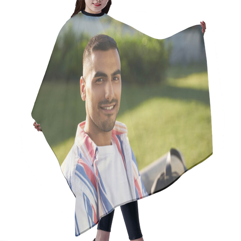 Personality  Portrait Of Handsome Smiling Middle Easter Student Looking At Camera  In University Campus. Happy Iranian Man Sitting On Bench, Relaxing In Park Hair Cutting Cape