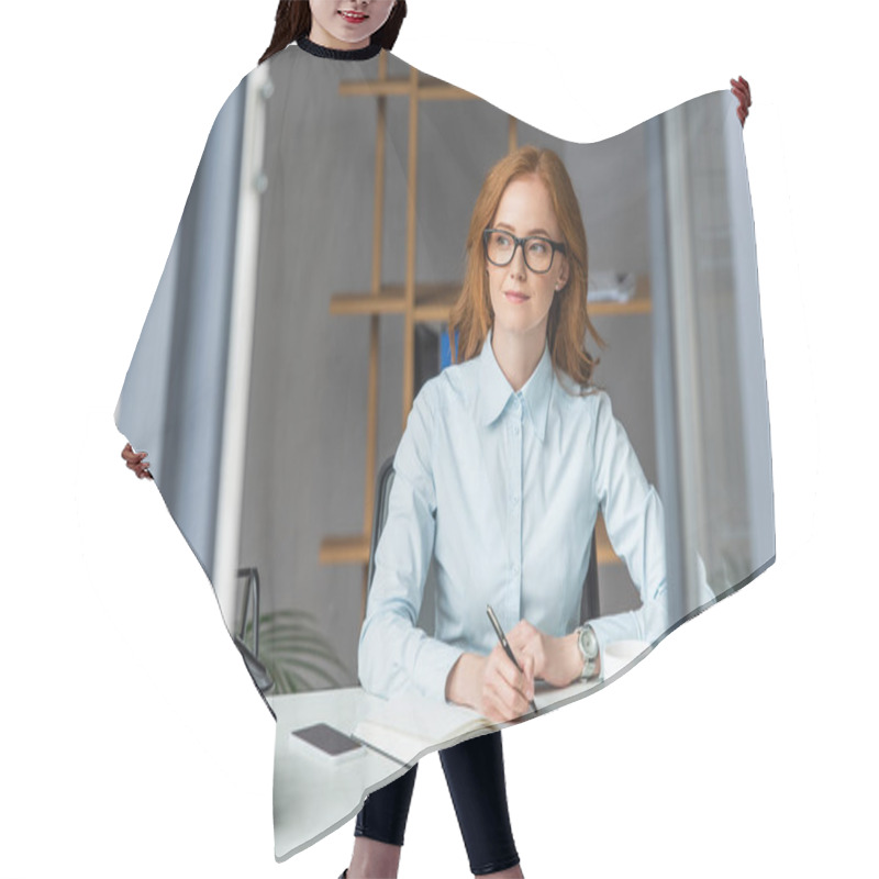 Personality  Positive Businesswoman Writing In Notebook, While Looking Away At Workplace With Blurred Window On Foreground Hair Cutting Cape