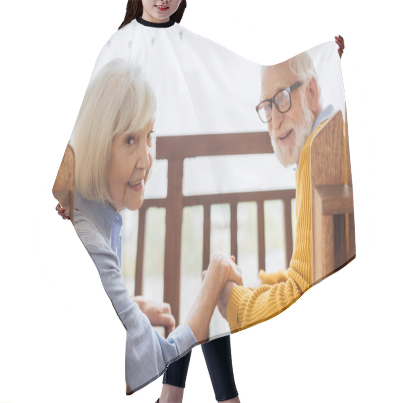 Personality  Smiling Elderly Couple Looking At Camera And Holding Hands While Sitting In Armchairs On Terrace On Blurred Background Hair Cutting Cape