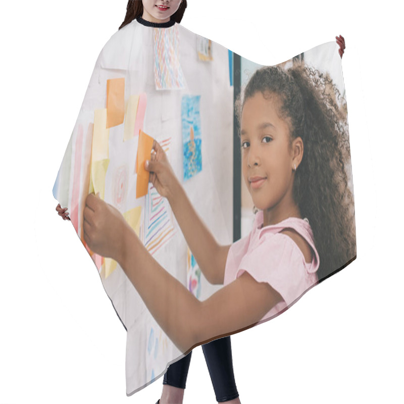 Personality  Side View Of African American Child Looking At Camera While Hanging Colorful Picture On White Wall In Room Hair Cutting Cape