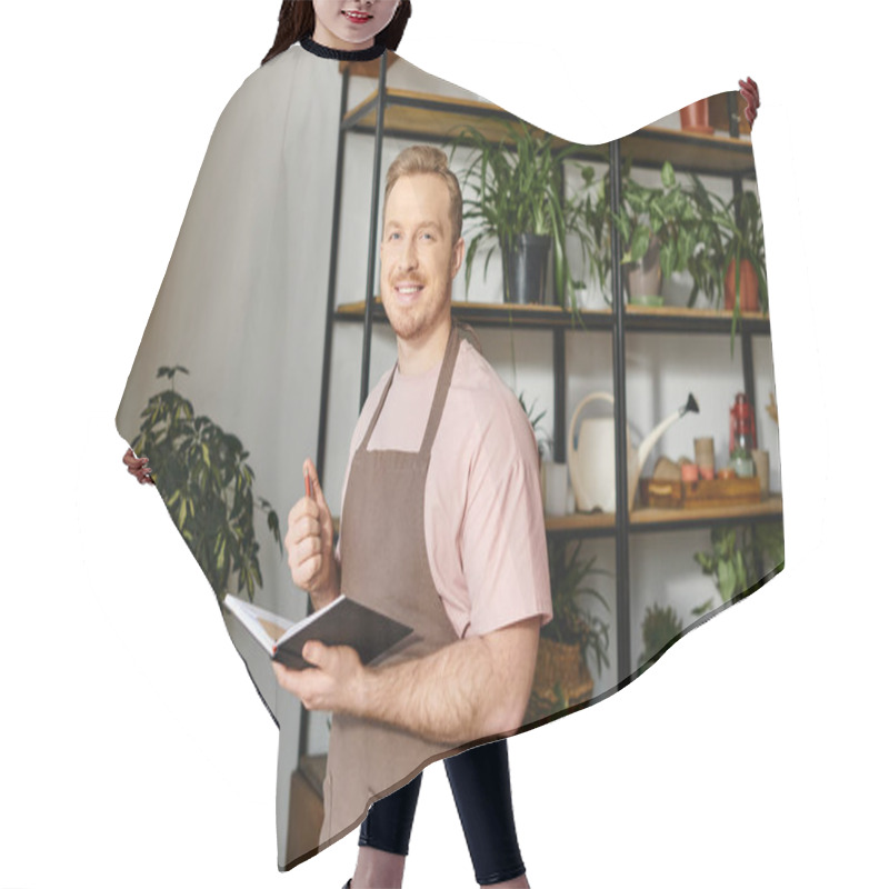 Personality  A Handsome Man In An Apron Holds A Notebook, Managing His Plant Shop With A Business Owners Dedication. Hair Cutting Cape