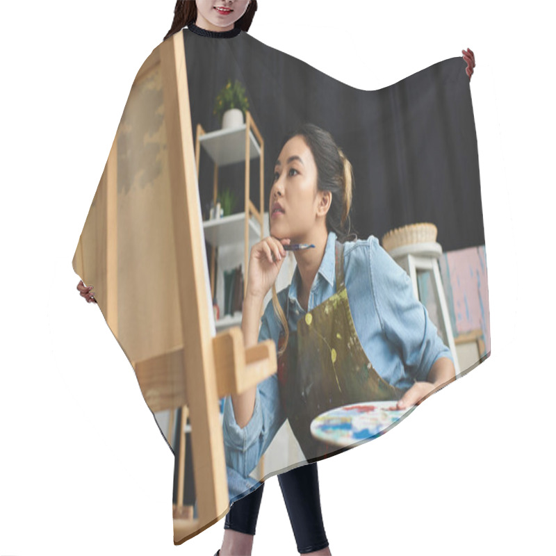 Personality  A Young Asian Woman, Wearing An Apron, Sits In Her Art Studio And Thoughtfully Contemplates Her Next Brushstroke On A Canvas. Hair Cutting Cape