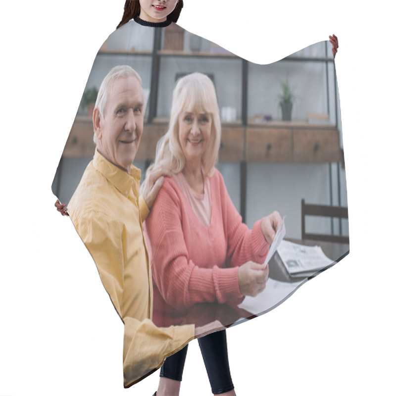 Personality  Happy Senior Couple Looking At Camera While Sitting At Table With Documents Hair Cutting Cape