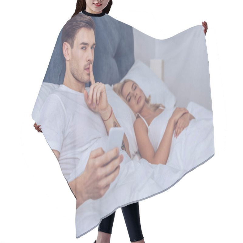 Personality  Man With Smartphone Gesturing For Silence And Looking At Camera While Lying With Sleeping Wife In Bed Hair Cutting Cape