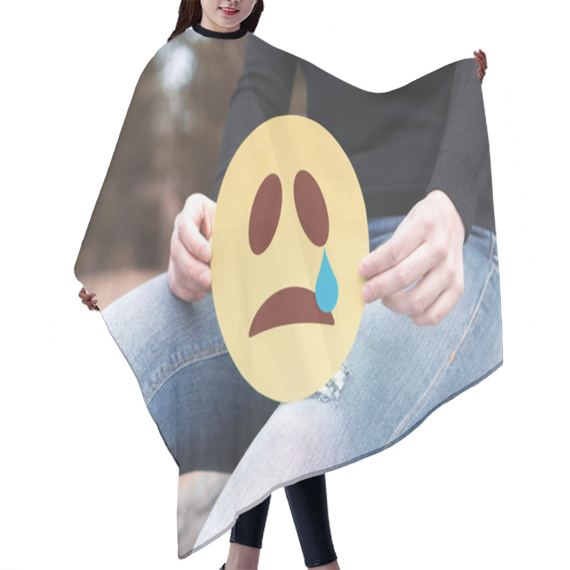 Personality  Sad Paper Emoticon In Hand. Depressed Woman Holding Printed Crying Smiley Face And Sitting On A Rock. Modern Communication And Smiley Icon On Cardboard. Sadness, Depression And Emotions Concept. Hair Cutting Cape