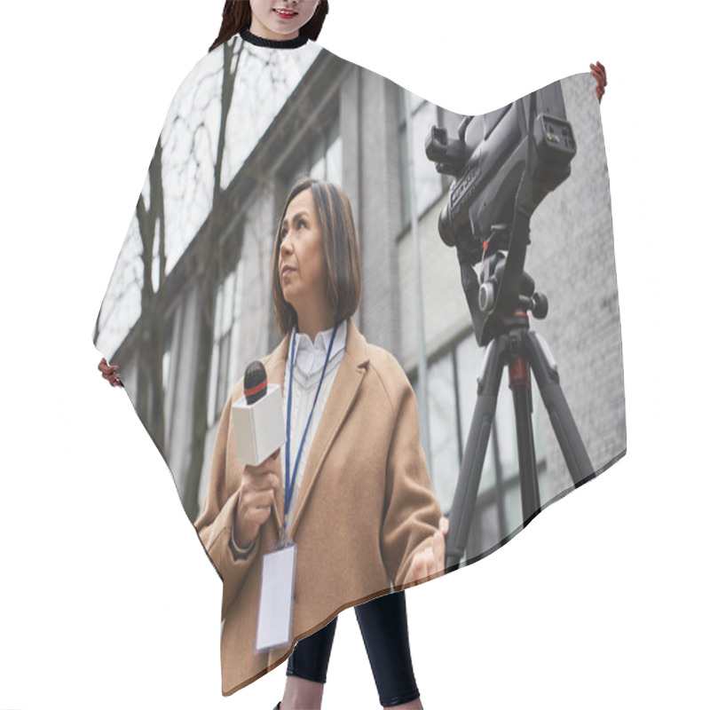 Personality  A Multiracial Female Journalist In A Beige Coat Holds A Microphone And Prepares To Report Outdoors. Hair Cutting Cape