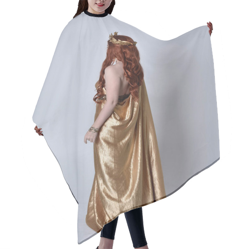 Personality  Full Length Portrait Of Girl With Red Hair Wearing Long Grecian Toga And Golden Wreath. Standing Pose With Back To The Camera,  Isolated Against A Grey Studio Background. Hair Cutting Cape