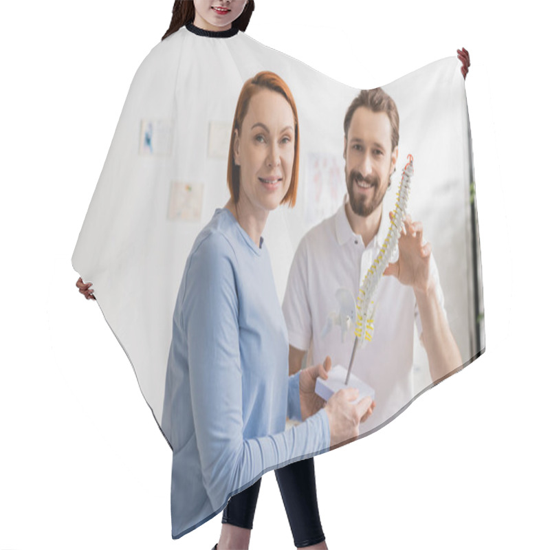 Personality  Cheerful Redhead Woman And Bearded Chiropractor Looking At Camera Near Spine Model In Consulting Room Hair Cutting Cape