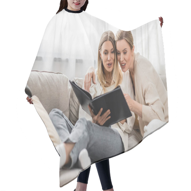 Personality  Surprised Blonde Sisters In Trendy Outfit Looking At Photo Album On White Curtain Backdrop, Bonding Hair Cutting Cape