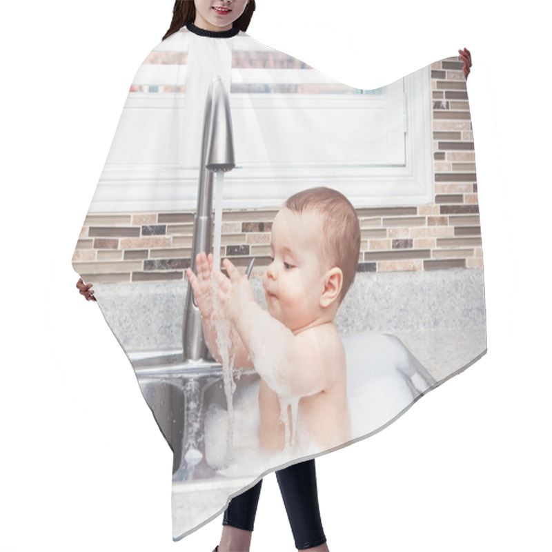 Personality  Portrait Of Cute Caucasian Funny Baby Girl Boy With Dark Black Eyes Sitting In Big Kitchen Sink With Water And Foam  Near Window Looking Away, Lifestyle Everyday Concept Hair Cutting Cape