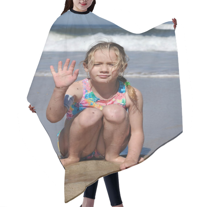 Personality  The Child Sits On The Background Of The Atlantic Ocean And Waves His Hand At The Camera. A Seven-year-old Girl Sits On The Beach And Smiles. Hair Cutting Cape