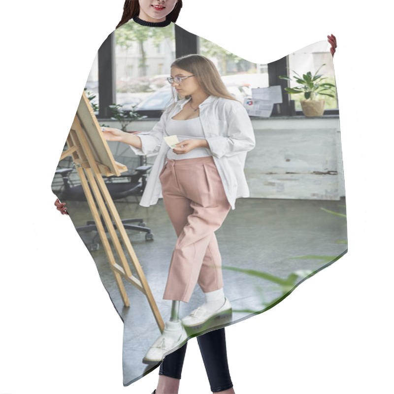 Personality  A Young Woman With A Prosthetic Leg Examines Her Canvas While Standing In A Studio. Hair Cutting Cape